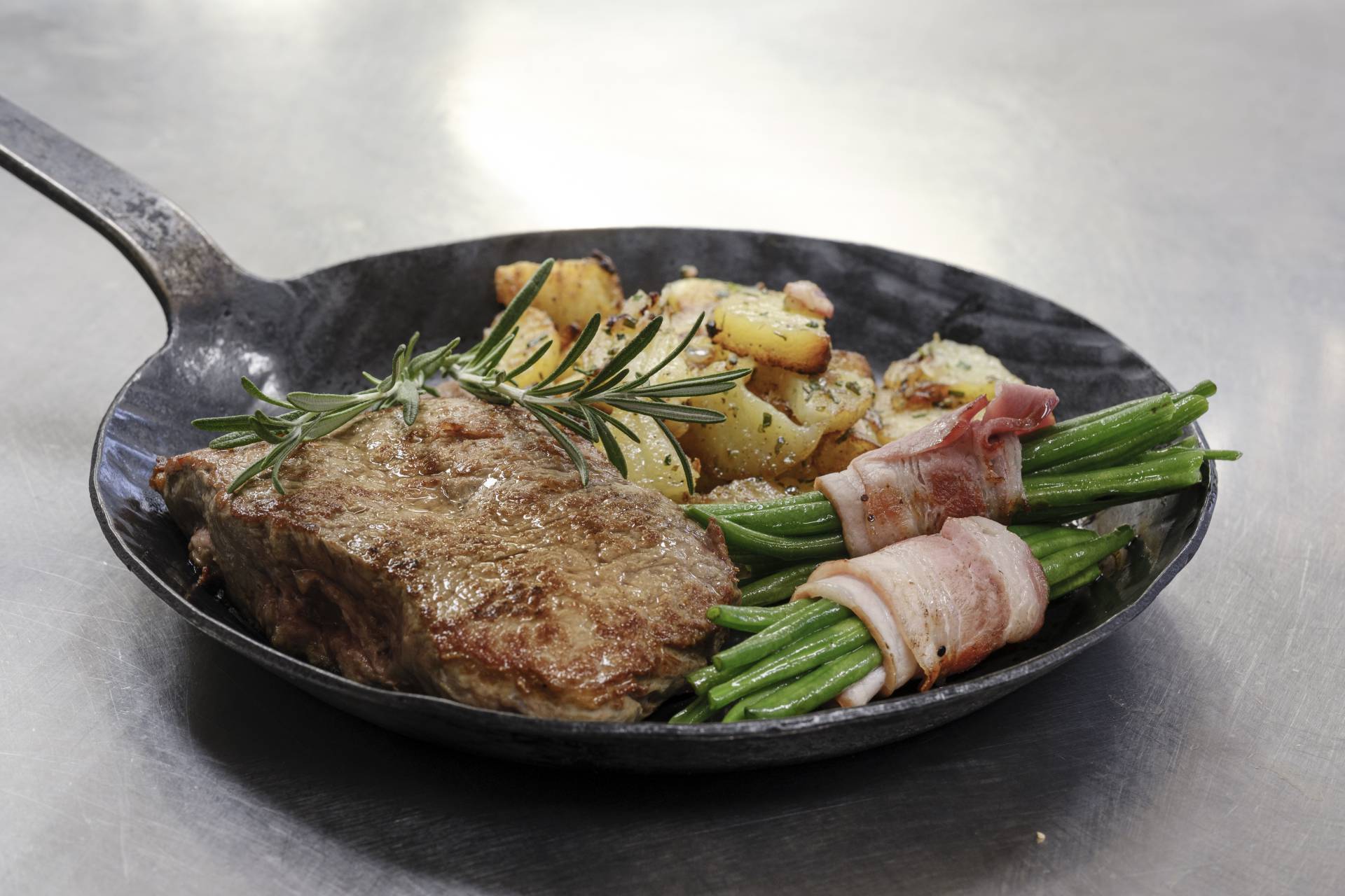 Gußeiserne Pfanne mit Steak, Kartoffeln und Bohnen im Speckmantel