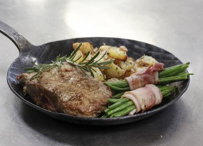 Gußeiserne Pfanne mit Steak, Kartoffeln und Bohnen im Speckmantel